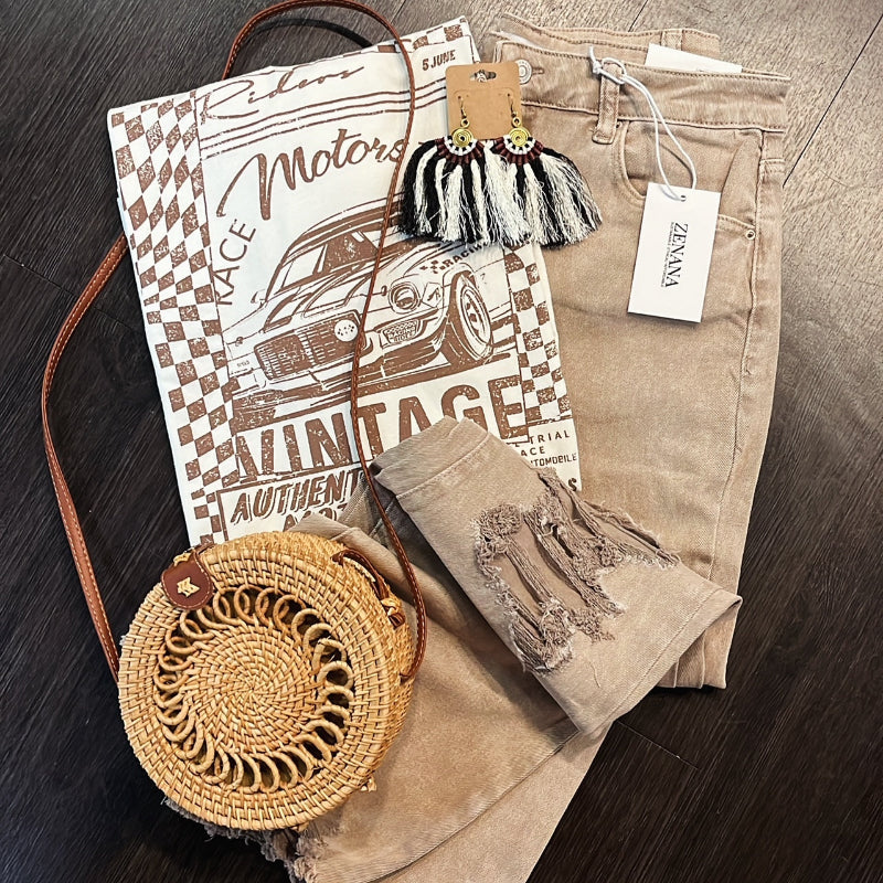 Flat lay of boutique outfit featuring vintage graphic tee, distressed jeans, woven crossbody bag, and artisan earrings from Emporium 23.