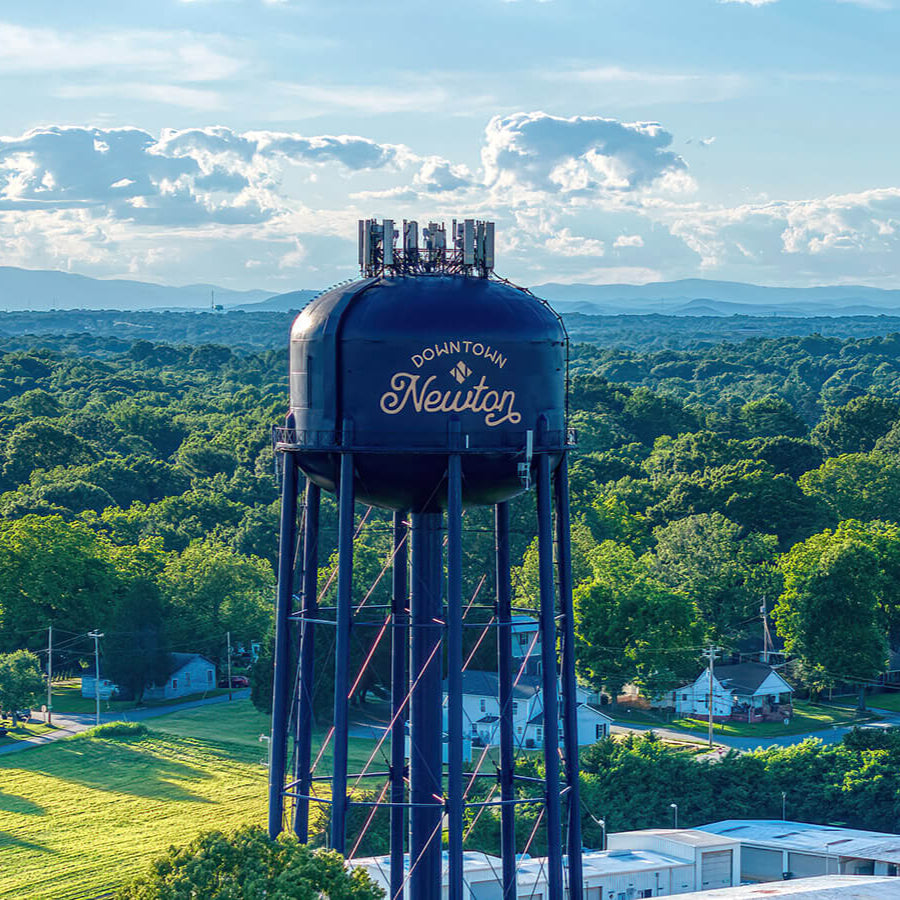 Aerial view of the Downtown Newton NC water tower with Blue Ridge Mountains in the background, representing the local community near Emporium 23.