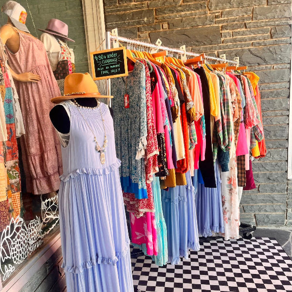 Outdoor boutique display of women’s dresses and colorful apparel rack with clearance sale sign – Emporium 23 fashion in Newton NC.